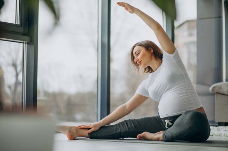 trudnica radi vežbe joge na podu pored prozora